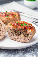 Low carb paleo meat cups, stuffed with champignons, bacon and cheese, garnished with green onion, on a white plate, vertical, closeup