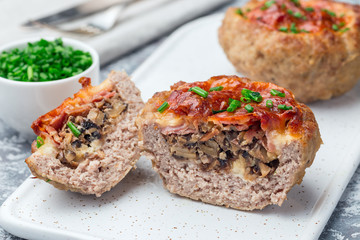  Low carb paleo meat cups, stuffed with champignons, bacon and cheese, garnished with green onion, on a white plate, horizontal