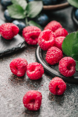 Fresh berries with raspberries, blueberries, blackberries in bowl on a stone stand on a dark metal background.