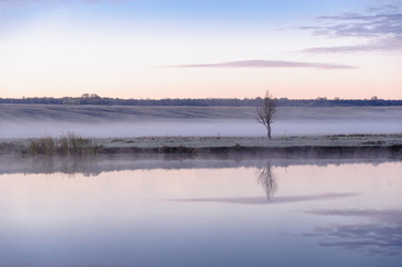 Dawn over the river on a summer morning, fog over the field, grass with hoarfrost