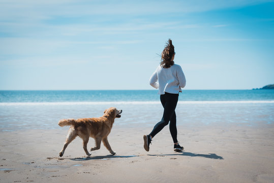 Fit Young woman running with her dog on the beach