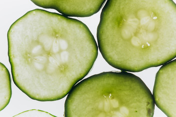 green translucent slices of cucumber on the background of bright white light close-up. transparent discs of vegetables. texture of kaleidoscope patterns in macro