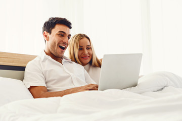 Couple caucasian lover smiling showing very happy gesture while enjoy using laptop computer together on bed early morning