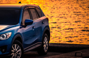 Blue compact SUV car with sport and modern design parked on concrete road by sea at sunset. Environmentally friendly technology. Hybrid and electric car technology. Car parking space. summer travel.