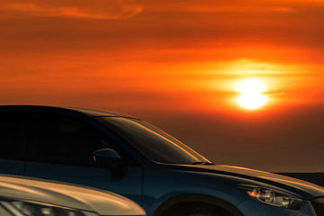 Side view of blue SUV car with sport and modern design parked on concrete road at sunset. Hybrid and electric car technology. Road trip. Automotive industry. Car parking lot with beautiful sunset.