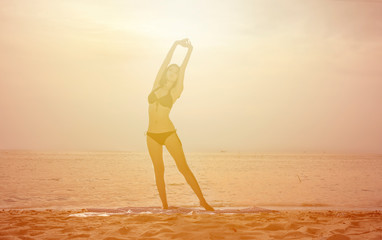 Fototapeta na wymiar Slip women with Bikini standing warm up body on beach with sunray