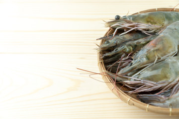close up group of fresh raw pacific white shrimp in bamboo bowl on wooden table.