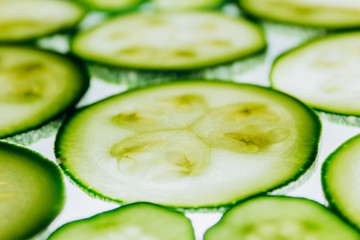 green translucent slices of cucumber on the background of bright white light close-up. transparent...
