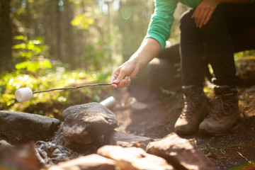 A girl sits by the fire in the woods drinking tea and roasting marshmallows