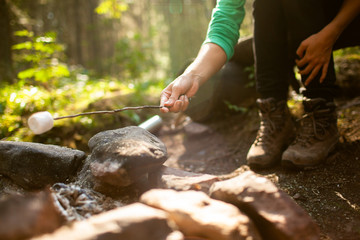 A girl sits by the fire in the woods drinking tea and roasting marshmallows