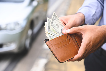 Businessman holding a wallet in the hands and take money out of pocket on car background.