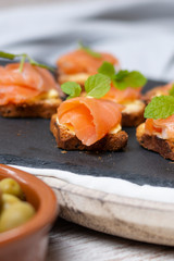 Smoked salmon on toast with butter with mint leaf on black stone and old wooden board - image
