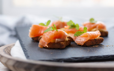 Smoked salmon on toast with butter with mint leaf on black stone and old wooden board - image