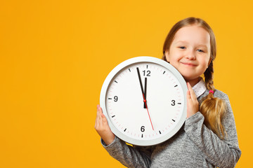 Little girl with pigtails holds a big clock on a yellow background. The concept of education,...