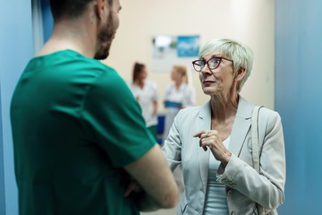 Senior woman talking to a surgeon in hospital hallway.
