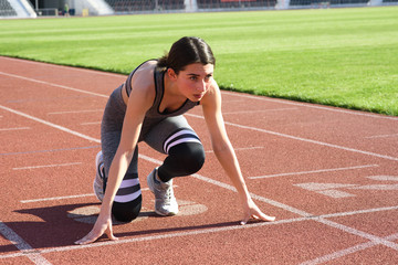 Young beautiful woman runner outdoor standing in start pose at the stadium