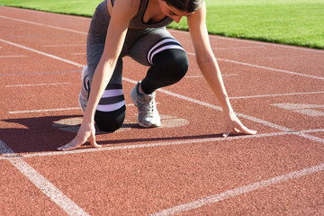 Young beautiful woman runner outdoor standing in start pose at the stadium
