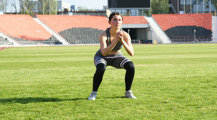 Fototapeta premium Beautiful athletic girl crouches on the grass in the stadium