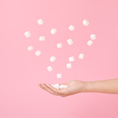 Sugar cubes in hand and flying sugar cubes in heart shape on pastel pink.