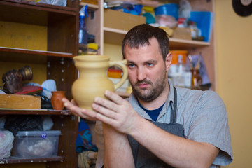 Professional male potter examining jar in pottery workshop