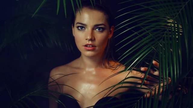 Beautiful girl with tanned skin poses and walks among tropical plants. Natural makeup and wet hair in a girl amazon. Natural cosmetics, spa procedures.