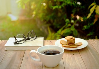 a cup of hot coffee on wooden table in green garden.