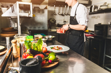Professional chef cooking in the kitchen restaurant at the hotel, preparing dinner. A cook in an apron makes a salad of vegetables and pizza.