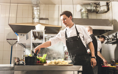 Professional chef cooking in the kitchen restaurant at the hotel, preparing dinner. A cook in an...