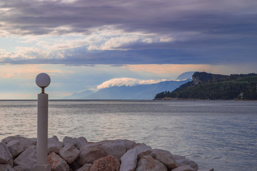 A cloudy sky at a shoreline. Te clouds are floating over the mountains at the side of the sea