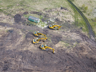 Aerial view of four yellow crawler excavators that stand on the ground near the construction site...