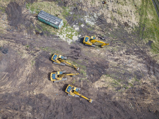 Aerial top view of four yellow crawler excavators standing on ground near the construction site and...
