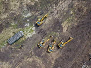 Aerial top view of four yellow crawler excavators standing on ground near the construction site and...