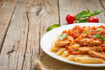 Penne pasta, chicken or turkey fillet, tomato sauce with basil leaves on old rustic wooden background. Copy space, side view, close up