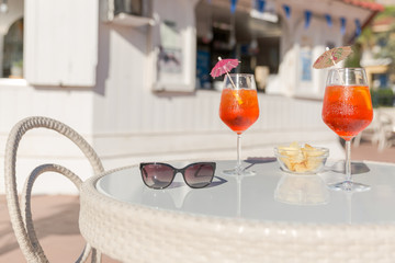 Two aperol spritz cocktails , chips and sunglasses on a table in an outdoor bar. Appetizer for two....