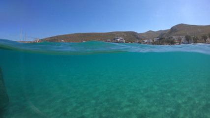 Fototapeta na wymiar Underwater sea level photo of idilic pebble beach of Karavostasis, picturesque port of Folegandros island with traditional fishing boats docked and crystal clear turquoise sea, Cyclades, Greece