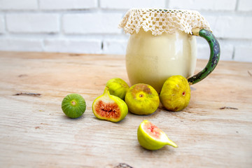 Over ripe and halved figs together with an antique enamel jug and lace doily on a raw wood surface