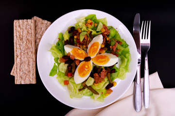 Tuna salad with lettuce, eggs and tomatoes with breads on black table. Diet menu. Top view. Restaurant salad menu concept. Food bloggers background.