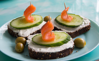 Sandwich with red fish, cucumber, cottage cheese and olives on a plate