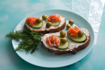 Sandwich with red fish, cucumber, cottage cheese and olives on a plate