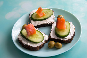 Sandwich with red fish, cucumber, cottage cheese and olives on a plate