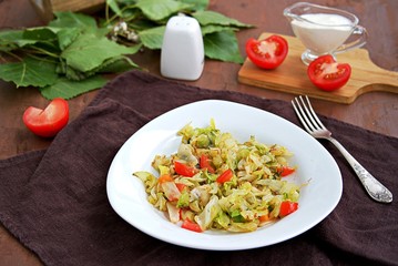 Fried cabbage with tomatoes in a white plate on a dark brown background. Served with sour cream.
