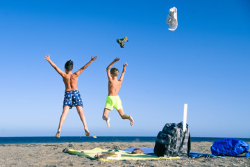 Students jump happy on the beach after the end of school.  Two boys throw clothes jumping and running in the ocean to taking bath Concept of freedom and happiness. Schoolmates enjoying summer vacation