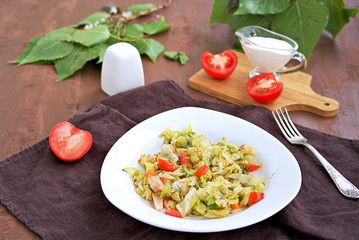 Fried cabbage with tomatoes in a white plate on a dark brown background. Served with sour cream.