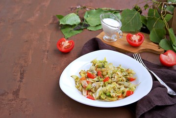 Fried cabbage with tomatoes in a white plate on a dark brown background. Served with sour cream.