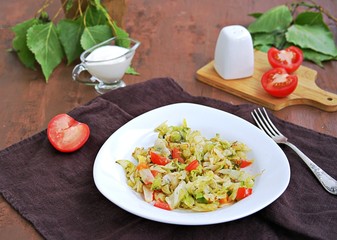 Fried cabbage with tomatoes in a white plate on a dark brown background. Served with sour cream.