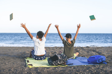 Students happy on the beach celebrate the end of the school throwing books Two excited boys playing together near the sea Concept of freedom and happiness. Schoolmates enjoying holiday summer vacation