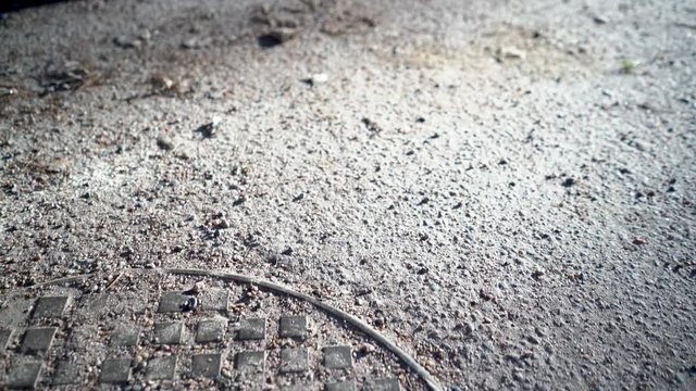 Footage of manhole cover covered with gravel, surface is asphalt, shot with gimbal and full frame camera moving to back and left, shallow depth of field, bokeh