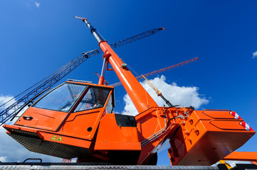 Mobile construction crane with telescopic arm mounted on truck with orange bodywork and big tower...