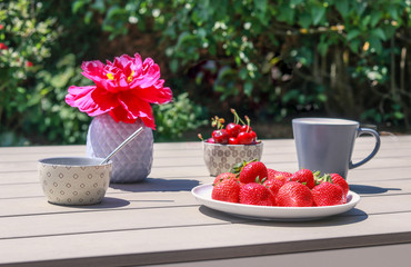 Breakfast in the garden at late summer morning. Strawberries and cherries. Hard light on terrace outdoors.