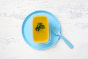 lentil soup in a plastic box on a plastic colored plate. on a white wooden table